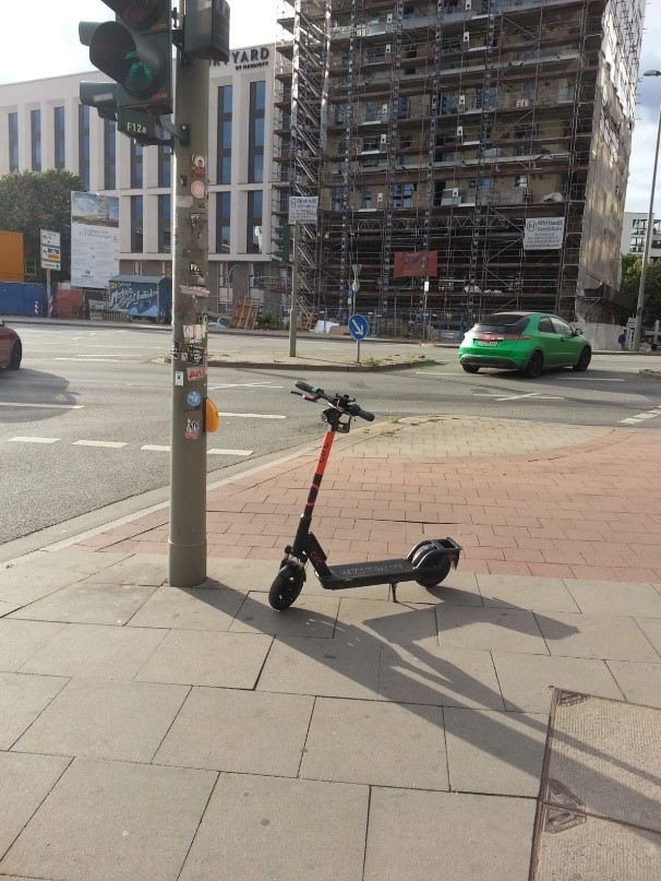 Auf dem Bild wurde ein E-Scooter direkt vor einer Ampel abgestellt und versperrt den Weg zum Anforderungstaster